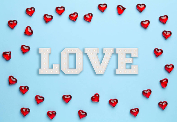 Fondo azul liso con marco hecho de pequeños corazones rojos y amor blanco dentro de él
 - Foto, imagen