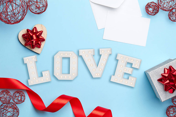Blue plain background with silver gift, red ribbon, white letter and love sign - Photo, Image