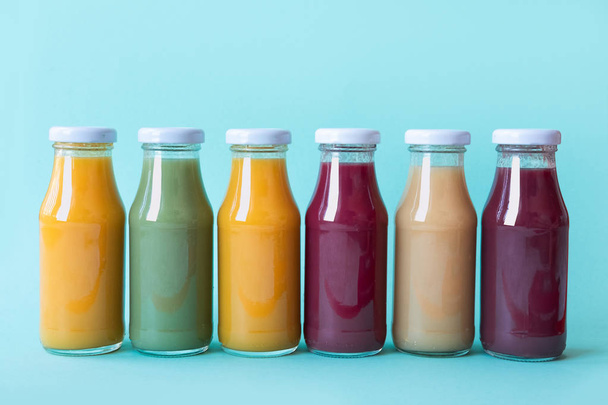 Raw vegetable and fruit juices in glass bottles on blue background - Valokuva, kuva