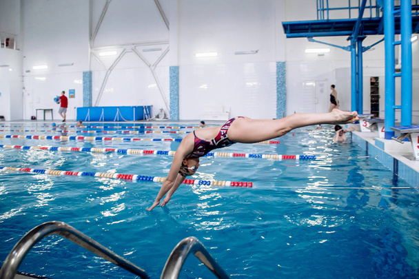 Tyttö uimari hyppää uima-altaaseen alkaen jalustat numero kuusi
 - Valokuva, kuva