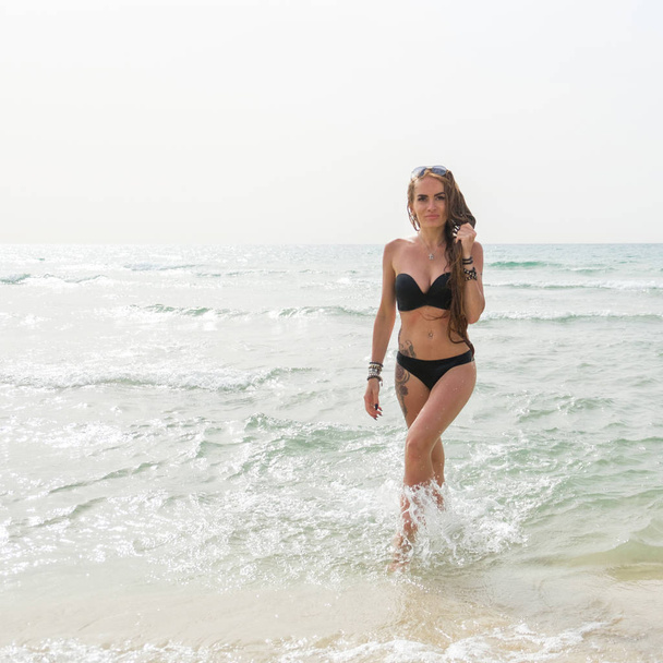 young beautiful girl in an open swimsuit bikini in sunglasses posing on the beach of the Mediterranean Sea - Фото, зображення