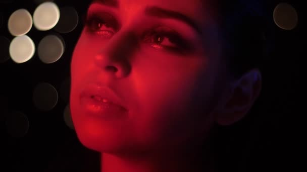 Closeup lő csinos női arc lenyűgöző divatos smink vörös Neonfény és bokeh háttérben pózol előtt a kamera a klubban - Felvétel, videó