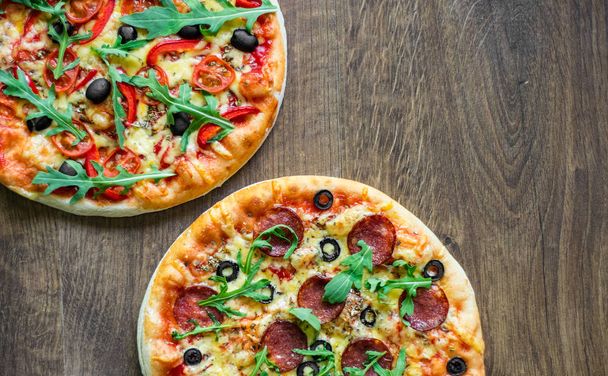 Pepperoni Pizza ja Pizza Mozzarella-juustolla, tomaateilla, pippurilla, oliivilla, mausteilla ja tuoreella arugulalla. Pizza Margherita tai Margarita puinen pöytä tausta
 - Valokuva, kuva