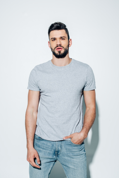 handsome bearded man looking at camera and standing with hand in pocket on white  - Fotoğraf, Görsel