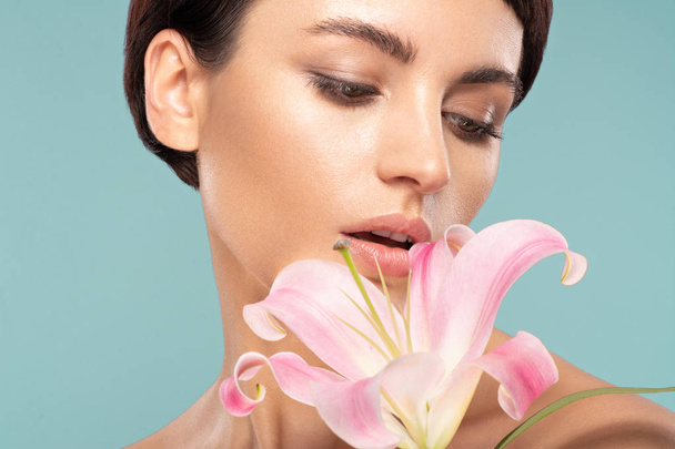 beautiful brunette with a short haircut and a pink lily  - Photo, Image