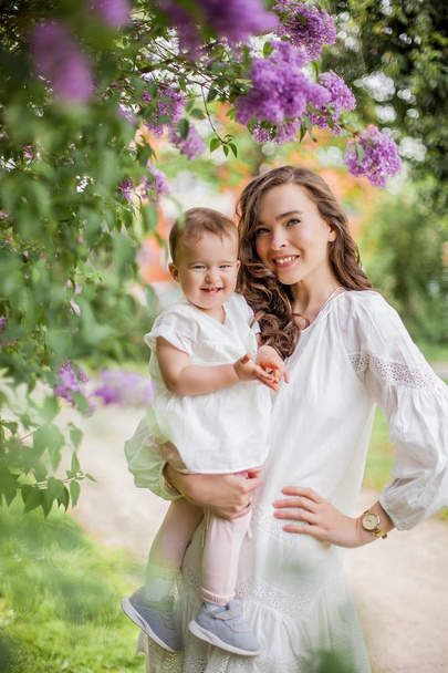 Beautiful young mother and little cute daughter are happy near the lilac. Portrait of mom and daughter. Spring. - Photo, image