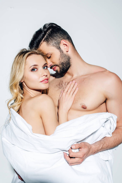 happy shirtless man holding blanket and looking at blonde nude girl on white  - Foto, immagini