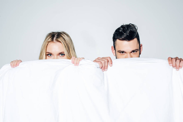 blonde woman and man looking at camera while covering face with blanket on white  - Photo, Image