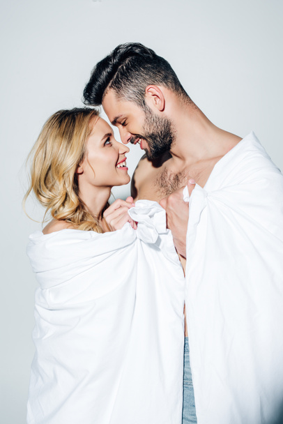 happy couple looking at each other while holding blanket on white  - Фото, изображение