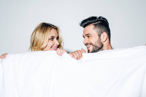 happy blonde woman and cheerful man looking at each other while holding blanket on white  - Foto, Imagem