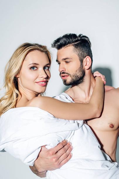 handsome shirtless man holding in arms cheerful blonde woman in blanket on white  - Photo, Image