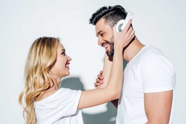 happy blonde girl touching headphones on cheerful bearded man on white  - Фото, зображення