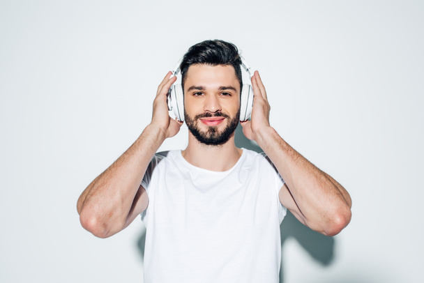 cheerful man touching headphones while listening music and smiling on white  - Foto, immagini