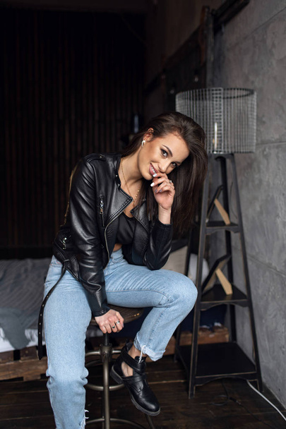 Sexy beautiful brunette in leather jacket and jeans posing in the room  - Foto, Imagem