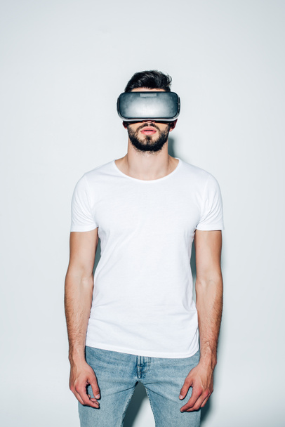 άντρας με γένια φορώντας ακουστικά εικονικής πραγματικότητας ενώ στέκεται πάνω σε λευκό  - Φωτογραφία, εικόνα