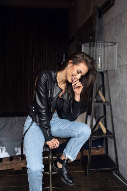 Sexy beautiful brunette in leather jacket and jeans posing in the room  - Foto, afbeelding