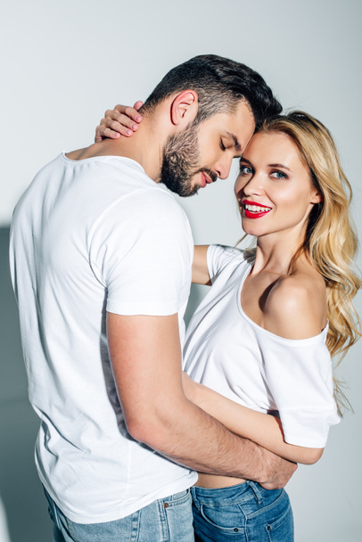 handsome man with closed eyes hugging cheerful blonde girl on white  - Фото, изображение