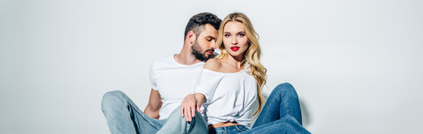 panoramic shot of handsome bearded man sitting and looking at attractive blonde girl on white  - Photo, Image