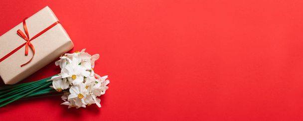 Federzusammensetzung. Strauß roter Blumen und Geschenkbox auf rotem Hintergrund. - Foto, Bild
