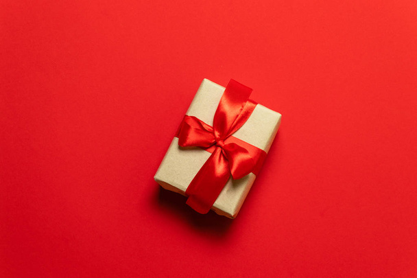 braune Geschenkschachtel mit roter Schleife auf rotem Tisch, Draufsicht - Foto, Bild