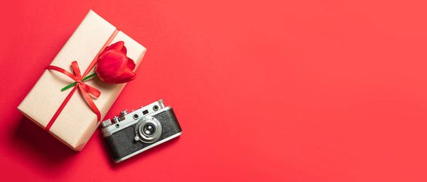 Κουτί δώρο έκπληξη με μια κόκκινη κορδέλα και μια τουλίπα σε κόκκινο φόντο - Φωτογραφία, εικόνα