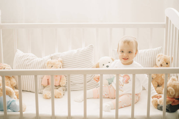 The toddler sits in a crib and plays. - Photo, Image