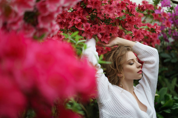 concept romantique printemps. jeune belle femme près des buissons azalées. dame dans les buissons en fleurs. femme en pull blanc et jupe corail
 - Photo, image