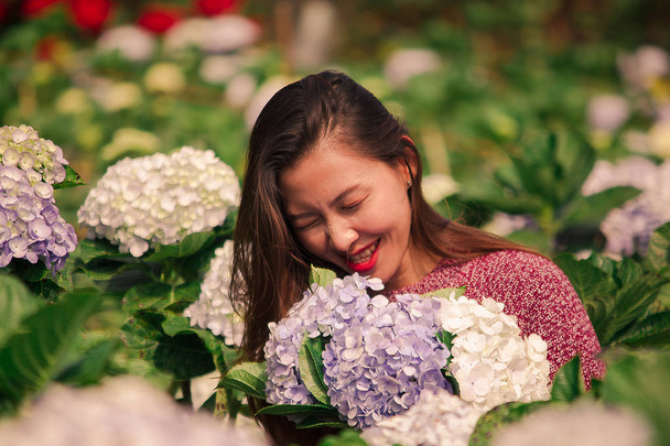 Una mujer con una camisa roja en un jardín de hortensias y divirtiéndose
 - Foto, Imagen
