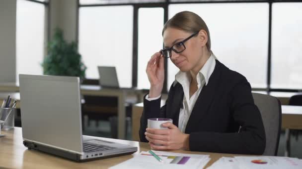 Businesswoman drinking coffee in office, having break, resting after work done - Filmati, video