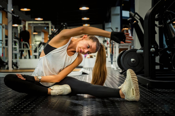 Beautiful female does stretching on the floor of gym - Fotó, kép