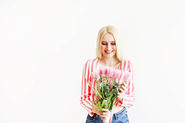 Young blonde woman in mom jeans and crop top shirt holding bouquet of tulips. - Foto, imagen