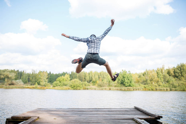Photo from back of jumping man on wooden bridge by river - Foto, Imagen