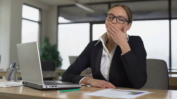 Woman yawning while reading on laptop, tired of monotonous work in office - Metraje, vídeo