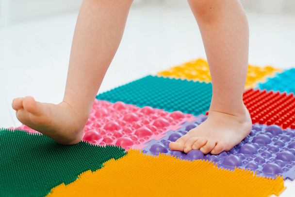 Toddler on baby foot massage mat. Exercises for legs on orthopedic massage carpet. prevention of flat feet and hallux valgus - Foto, immagini