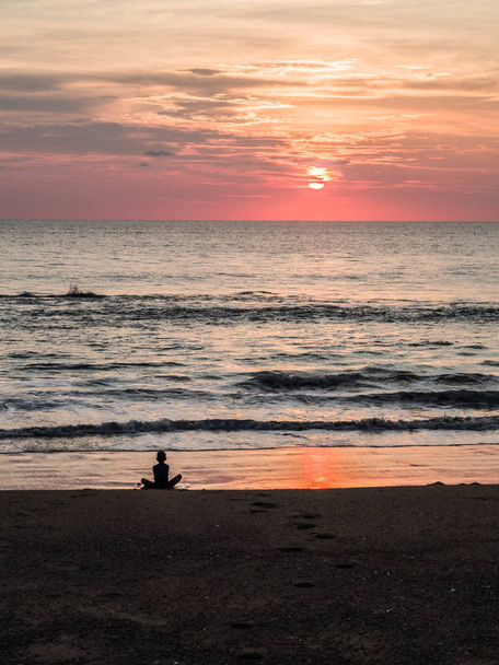 Силуэт неопределенного человека в положении лотоса на морском песчаном пляже во время красивого заката. Медитация на закате. Ребенок медитирует на вечернем морском пляже
. - Фото, изображение