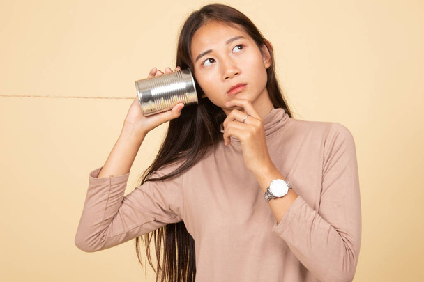 Young Asian woman hearing with tin can phone and thinking. - Fotoğraf, Görsel
