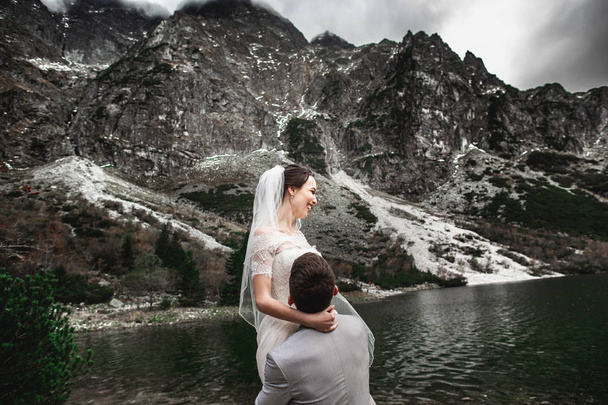 schöne Hochzeitsfotosession. umkreist der Bräutigam seine junge Braut am Ufer des Morskie oko-Sees. Polen - Foto, Bild
