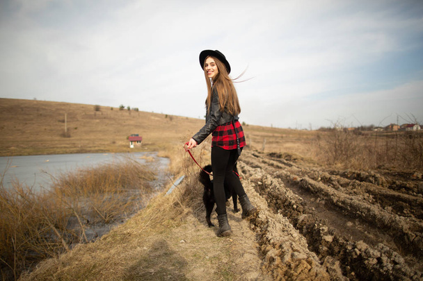 Ένα νεαρό κορίτσι περπατάει με ένα σκυλί στην όχθη μιας λίμνης. Πίσω όψη - Φωτογραφία, εικόνα