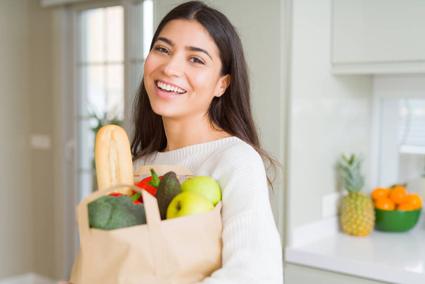 Beautiful young woman smiling holding a paper bag full of grocer - Photo, Image