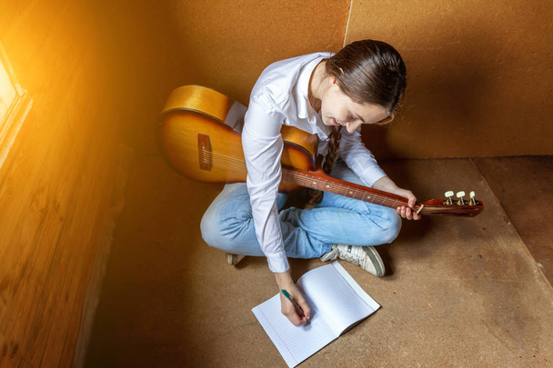 Νεαρή γυναίκα hipster κάθεται στο πάτωμα και παίζει κιθάρα στο σπίτι - Φωτογραφία, εικόνα