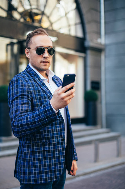 young stylish man holding a mobile phone in the city center. Man wearing jacket and shirt - Foto, Imagen