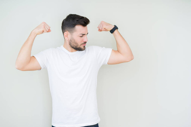 Young handsome man wearing casual white t-shirt over isolated background showing arms muscles smiling proud. Fitness concept. - Fotoğraf, Görsel