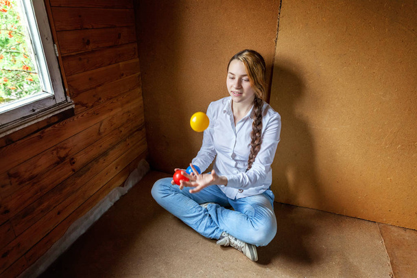 Молодая хипстерша сидит на полу и жонглирует цветными мячами дома.
 - Фото, изображение