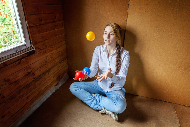 Jeune femme hipster assise sur le sol et jonglant avec des boules colorées à la maison
 - Photo, image