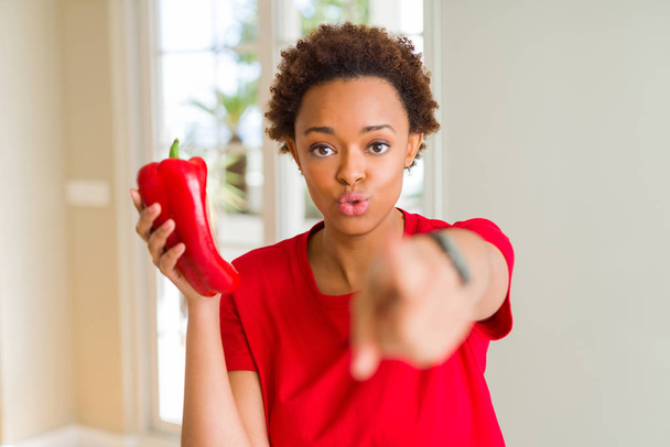 Młoda Afroamerykanka trzymająca świeżą czerwoną paprykę wskazującą palcem na kamerę i na ciebie, znak dłoni, pozytywny i pewny siebie gest z przodu - Zdjęcie, obraz