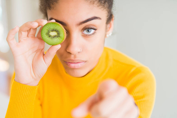 Jeune fille afro-américaine mangeant kiwi vert pointant du doigt vers la caméra et vers vous, signe de la main, geste positif et confiant de l'avant
 - Photo, image
