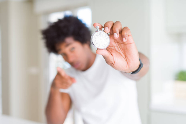 African American man holding stopwatch pointing with finger to the camera and to you, hand sign, positive and confident gesture from the front - Photo, Image