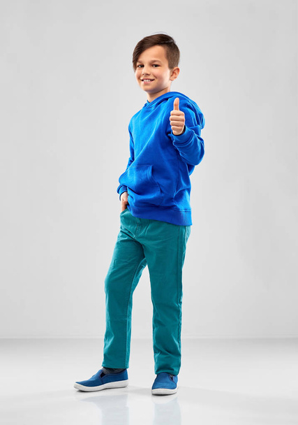 smiling boy in blue hoodie showing thumbs up - 写真・画像