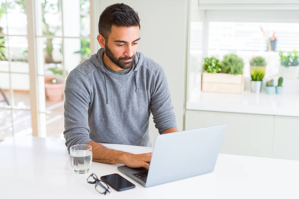 Hombre hispano guapo trabajando con computadora portátil con una expresión segura en cara inteligente pensando en serio
 - Foto, Imagen