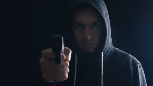 危険なフード付き犯罪者は黒い背景に彼の銃を目指しています - 映像、動画